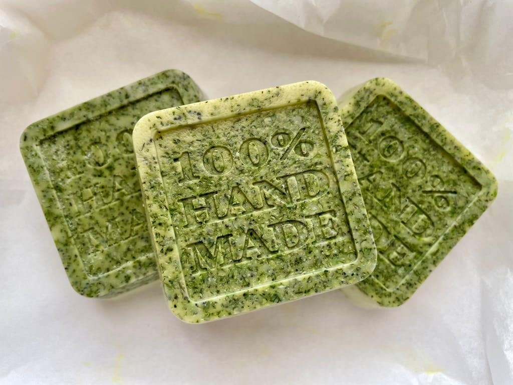 Three handmade organic green soap bars with 100% handmade text, set on white paper.