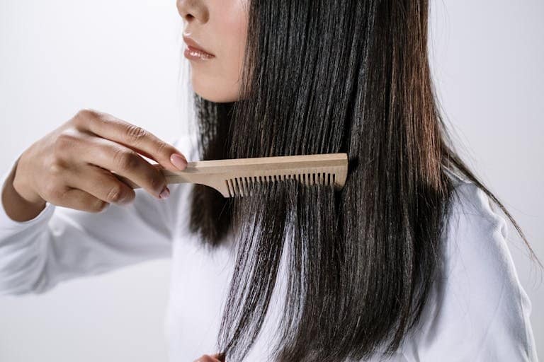 Close-up of a woman combing her hair with a wooden comb indoors, emphasizing hair care.